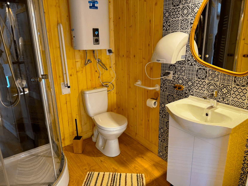 A bathroom equipped with a shower, toilet, sink, mirror, hand dryer, and accessible amenities for guests with disabilities.