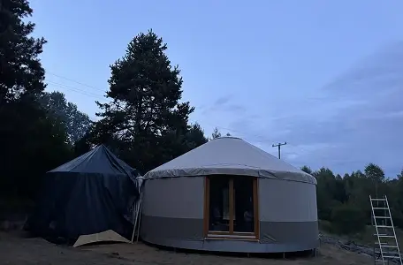 Ukończona jurta: Jurta z szarym, wodoodpornym pokryciem i drewnianymi drzwiami.