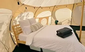 Wnętrze jurty z podwójnym łóżkiem, białą pościelą i ozdobnymi światełkami.