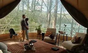 Stojąca para we wnętrz jurty w salonie z panoramicznym widokiem na las.