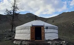 Zewnętrzny widok tradycyjnej białej jurty w suchym, górzystym krajobrazie.